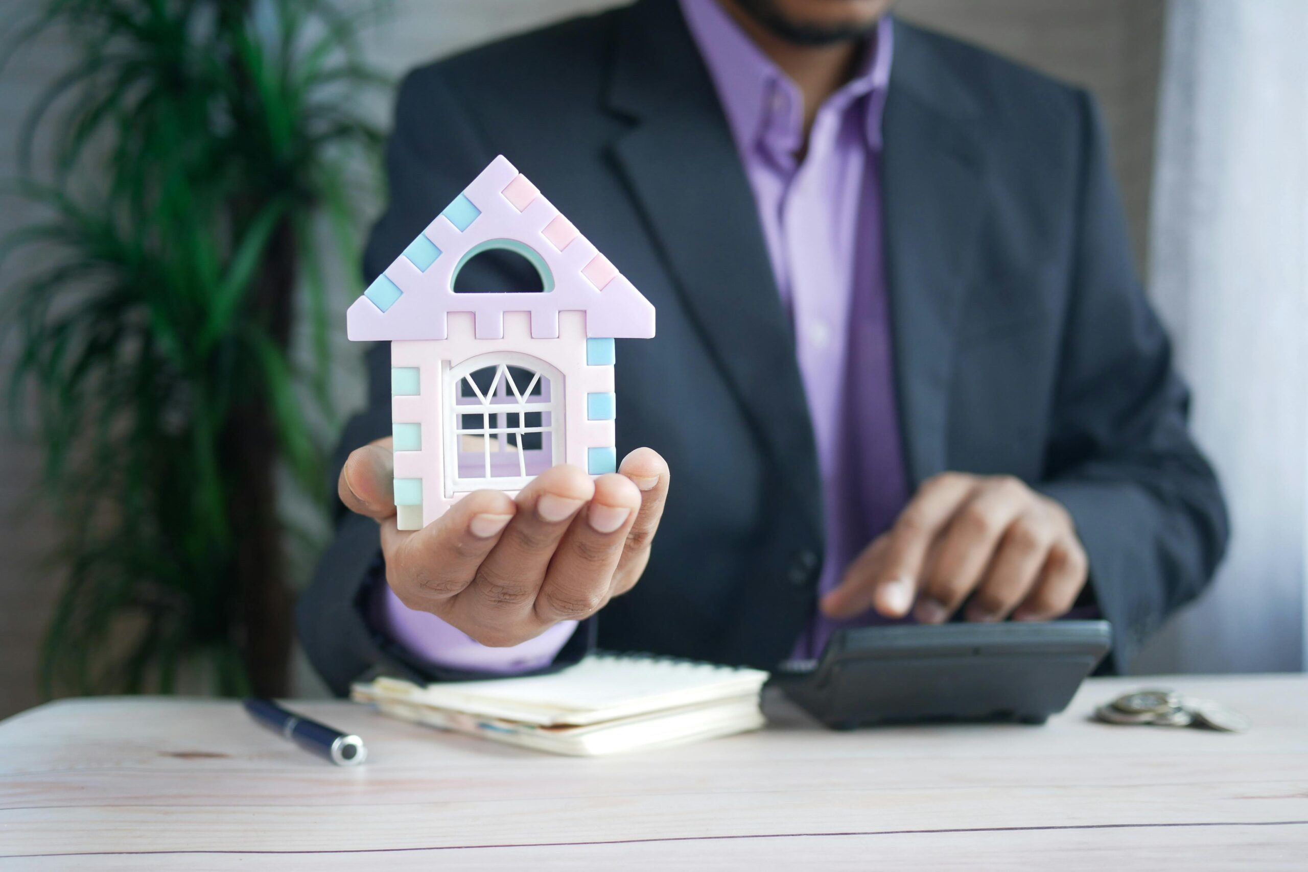 Businessman in suit holds model house, calculates real estate investments.